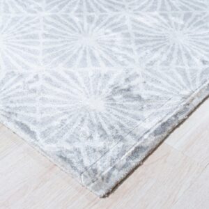 Close view of a gray plush rug featuring a repeating white geometric star pattern on pale wood flooring.