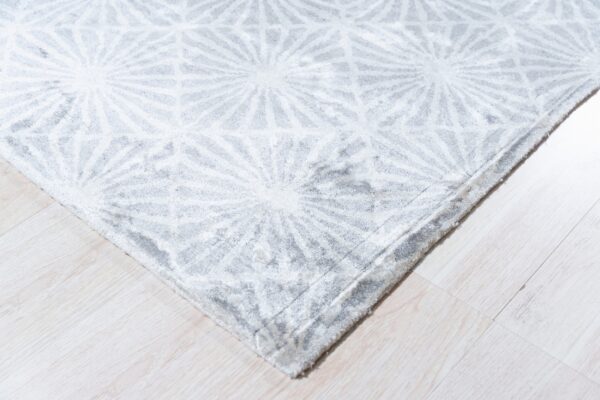 Close view of a gray plush rug featuring a repeating white geometric star pattern on pale wood flooring.