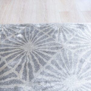 Plush gray and off-white rug displays an abstract radial geometric design over light wood planks.