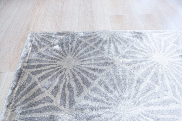 Plush gray and off-white rug displays an abstract radial geometric design over light wood planks.