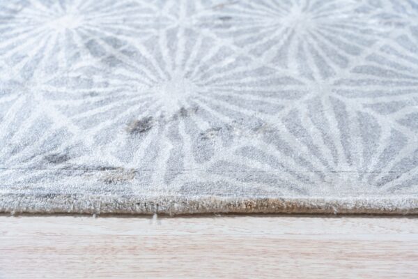 Close-up of a gray rug with a repeating white starburst geometric pattern resting on light wood flooring.