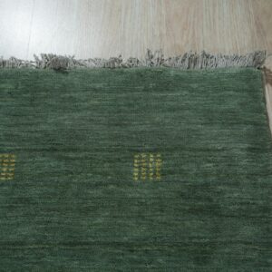 Dark green textured rug featuring small yellow square patterns and gray fringe resting on wood flooring.