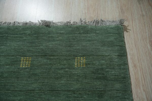 Dark green textured rug featuring small yellow square patterns and gray fringe resting on wood flooring.