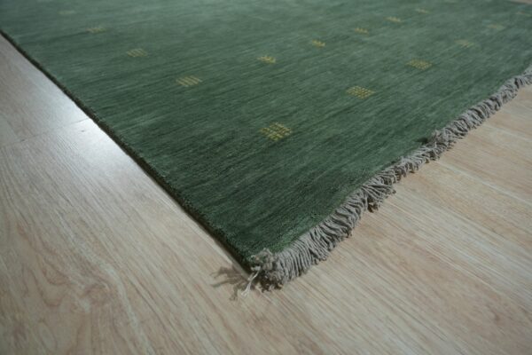 A dark green rug with small gold accent patterns and gray fringe rests on light wood flooring.