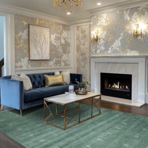 Teal low-pile rug with geometric accents anchors a room featuring a blue sofa and gold metallic wallpaper.