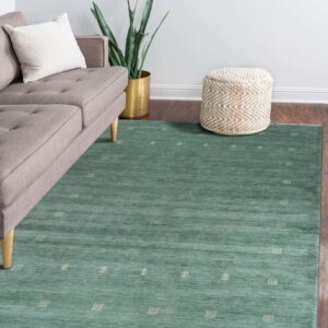 Teal low-pile rug with stylized beige geometric patterns complements a gray sofa on dark wood flooring.