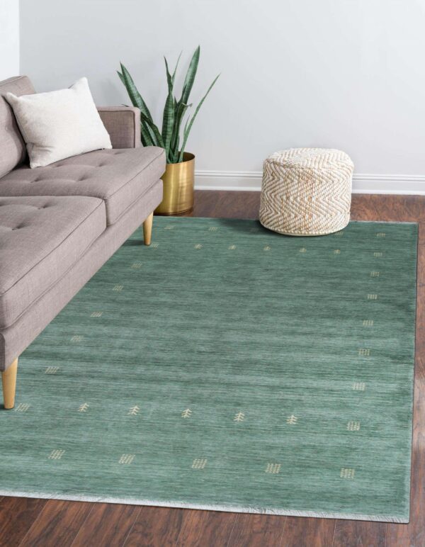 Teal low-pile rug with stylized beige geometric patterns complements a gray sofa on dark wood flooring.