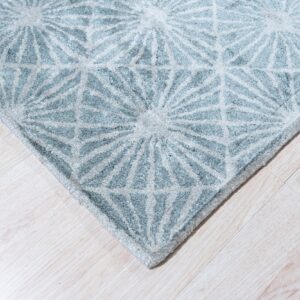 Light blue and gray high-pile rug with a repeating radial geometric design on pale wood planks.