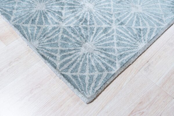 Light blue and gray high-pile rug with a repeating radial geometric design on pale wood planks.