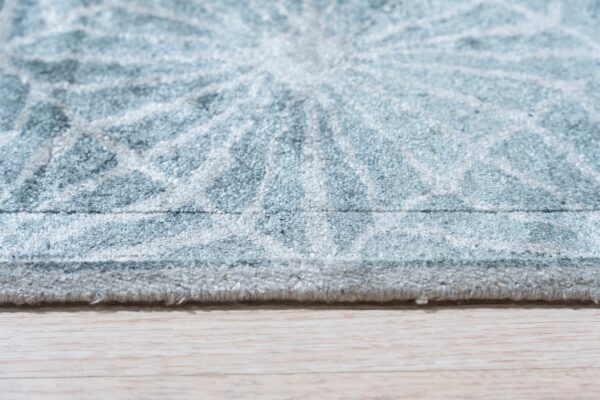 Textured light blue rug with an abstract radial pattern rests along the edge of a light wood floor.