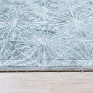 Textured, soft blue rug with a repeated white radial pattern rests on light blonde wood flooring.