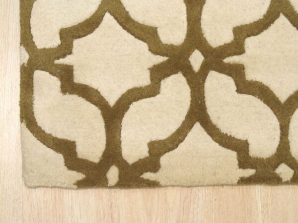 Close-up of a cut-pile rug featuring an ivory background and thick olive geometric lines on light wood flooring.