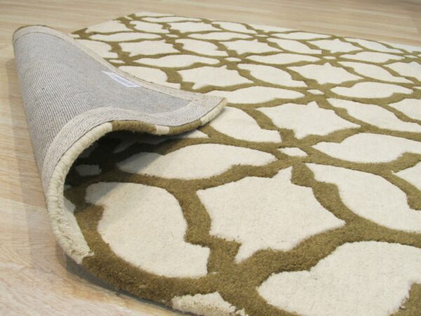 Cream rug with raised olive green geometric lattice pattern rolled back on light wood floor.