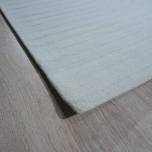 Close-up of a white, textured rug with carved concentric lines resting on light brown wood flooring.