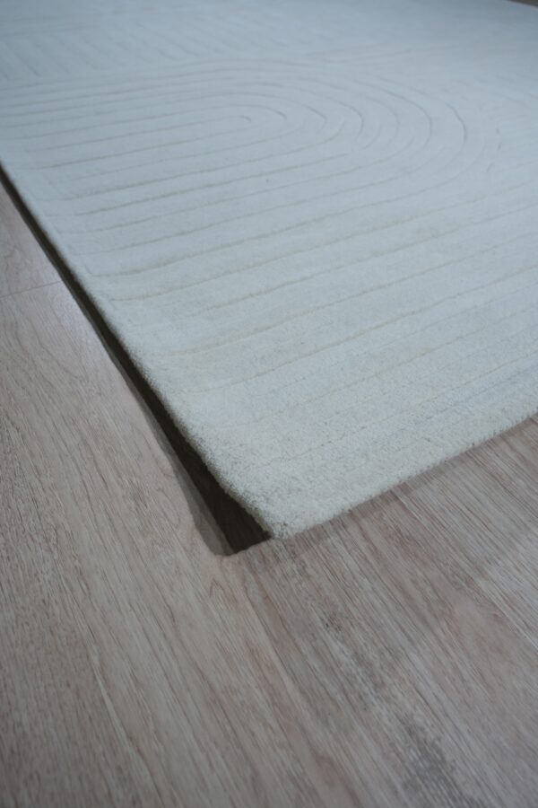 Close-up of a white, textured rug with carved concentric lines resting on light brown wood flooring.