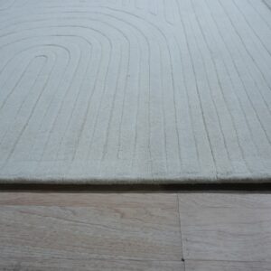 Off-white carved rug featuring concentric curved and parallel straight lines on light wood flooring.