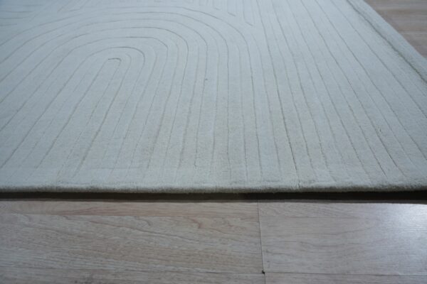 Off-white carved rug featuring concentric curved and parallel straight lines on light wood flooring.