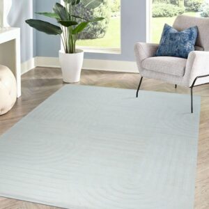 Pale gray rug featuring a carved geometric pattern lies on herringbone wood flooring near a light gray armchair.