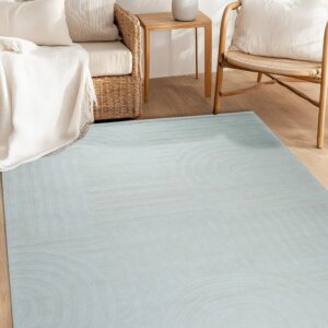 Dusty blue geometric carved rug anchors a bright space with natural wood flooring and rattan seating.
