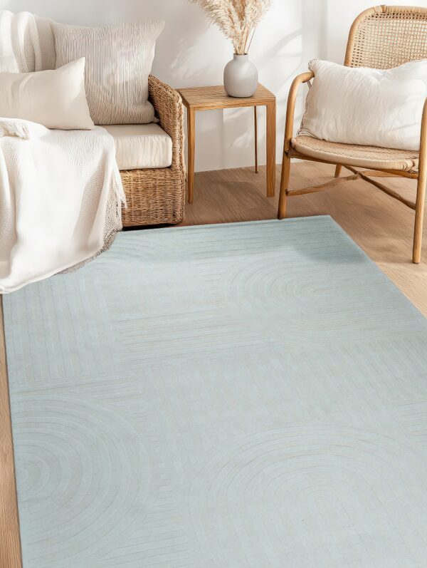 Dusty blue geometric carved rug anchors a bright space with natural wood flooring and rattan seating.