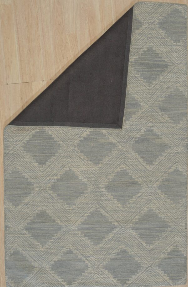 Low-pile blue-gray and cream diamond patterned rug on wood flooring with a dark gray backing exposed.