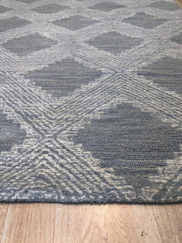 Textured gray and white rug with large diamond patterns lies on light wood planks.