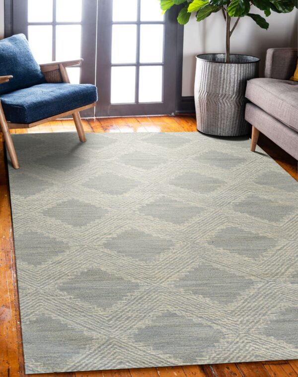 A low-pile gray and beige diamond pattern rug sits on hardwood floors between a blue chair and a gray sofa.