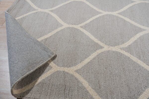Light gray rug with a beige geometric pattern, partially rolled back on light wood flooring.