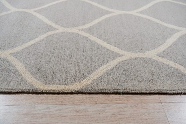 A close-up of a gray textured rug with a cream trellis pattern resting on glossy light wood planks.