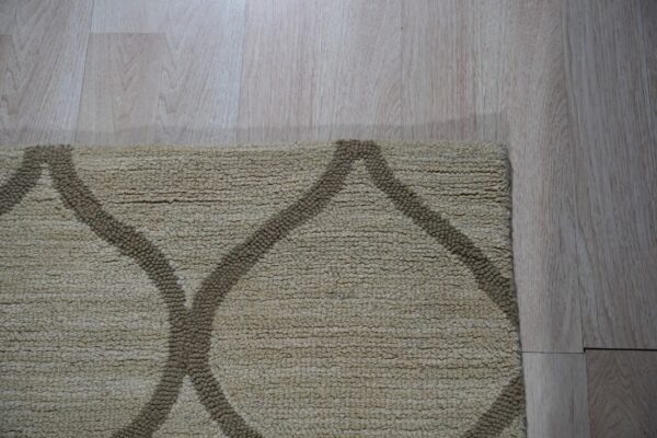 High-pile beige rug featuring a dark brown trellis pattern on light wood plank flooring.