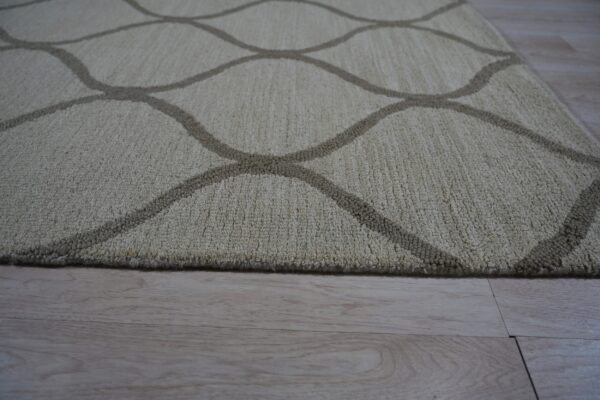 Beige textured rug featuring a contrasting curved lattice pattern rests on light wood floor.