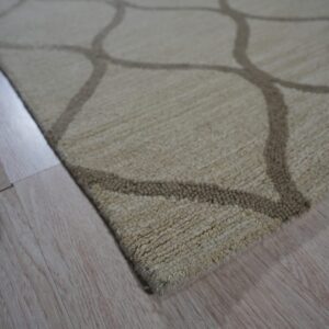 Textured beige rug with a dark geometric trellis pattern lying on light wood planks.