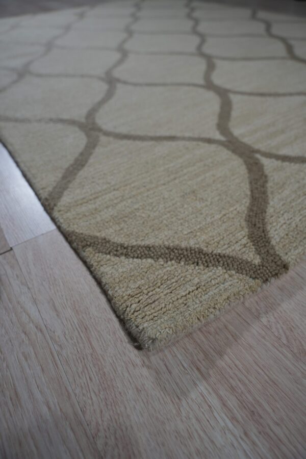 Textured beige rug with a dark geometric trellis pattern lying on light wood planks.