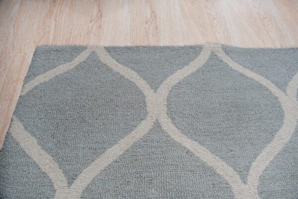 Textured blue and cream rug with an intersecting trellis pattern rests on light hardwood flooring.