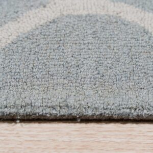 Low-pile rug in gray-blue with cream geometric arcs rests on light wood flooring.