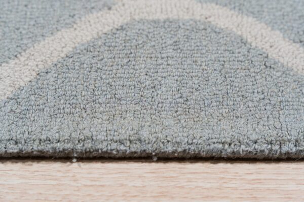 Low-pile rug in gray-blue with cream geometric arcs rests on light wood flooring.