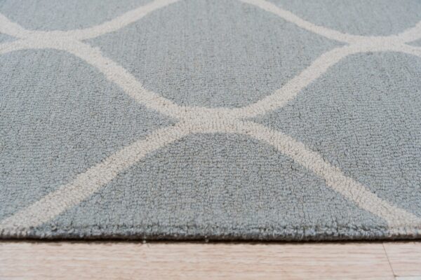 Low-angle detail of a textured blue-gray rug featuring a cream geometric trellis on wood floor.