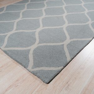 A dusty blue area rug featuring a light beige geometric trellis pattern rests on pale wood flooring.