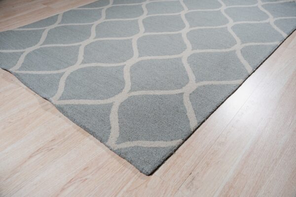A dusty blue area rug featuring a light beige geometric trellis pattern rests on pale wood flooring.