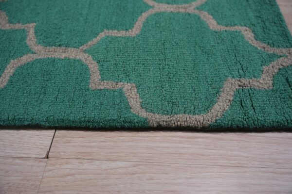 Textured green rug with a beige trellis pattern borders light blonde wood flooring.