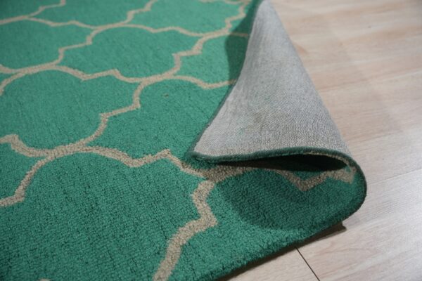 Teal quatrefoil pattern rug lifted to show the textured pile and gray woven backing on light wood flooring.