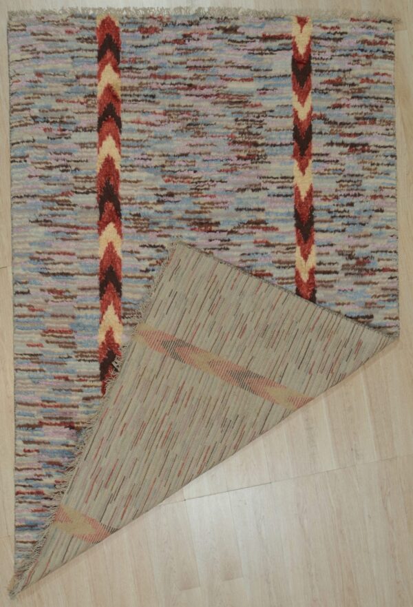 A shaggy blue and brown rug with chevron stripes is folded back on light wood plank flooring.