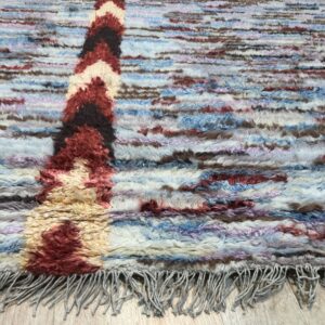 Shaggy blue, brown, and red patterned rug with fringe resting on light wood flooring.