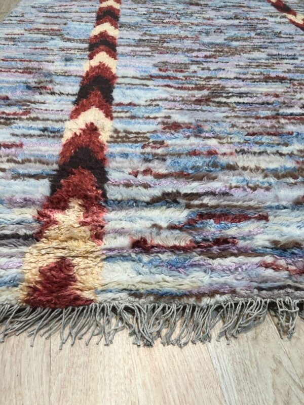 Shaggy blue, brown, and red patterned rug with fringe resting on light wood flooring.