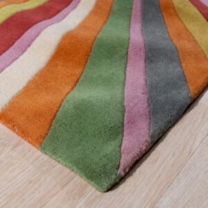 A low-pile rug featuring wide, wavy, multi-colored stripes rests diagonally across light wood flooring.