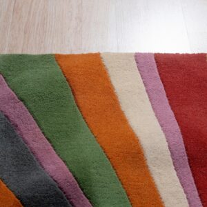 Multicolored rug corner with diagonal stripes of green, orange, red, cream, gray, and purple on wood planks.