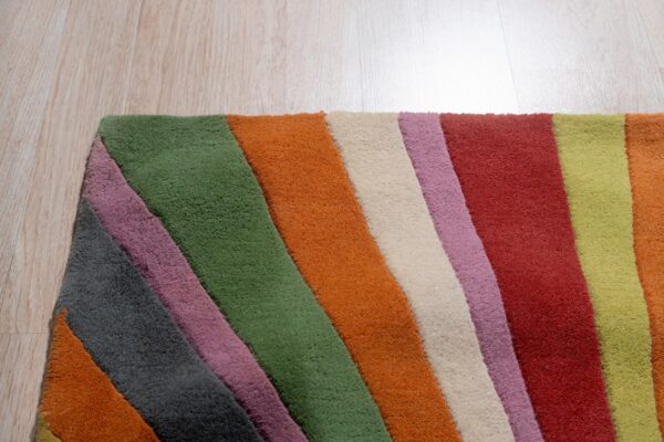 Multicolored rug corner with diagonal stripes of green, orange, red, cream, gray, and purple on wood planks.