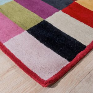 Plush multicolored rug with large geometric blocks of pink, black, and olive resting on light wood floors.