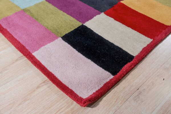 Plush multicolored rug with large geometric blocks of pink, black, and olive resting on light wood floors.