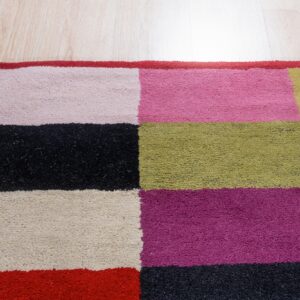 Colorful high-pile rug with geometric blocks of fuchsia, black, green, and beige on light flooring.